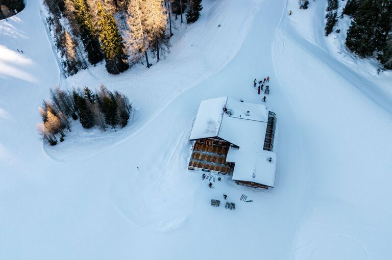 Holzhütte im Schnee mit Terrasse und abgestellten Skiern davor, umgeben von Bäumen. | © Mitterhausalm | Alpine Genusswelten