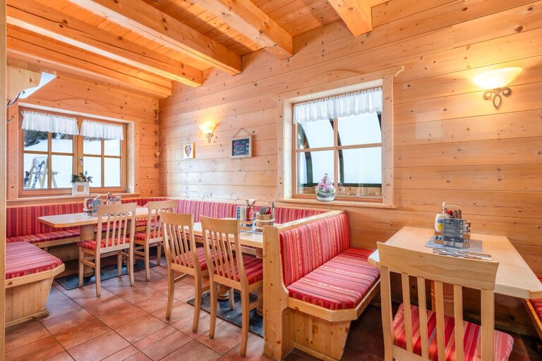 Gemütlicher Gastraum mit Holzwänden, roten Polsterbänken und Holztischen, warm beleuchtet. | © Mitterhausalm | Alpine Genusswelten