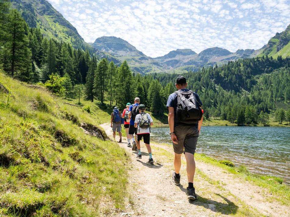 „Kinder und Erwachsene wandern entlang des Duizitzkarsees durch die alpine Landschaft mit Wald und Bergen.“ | © TVB/Laura Passenbrunner