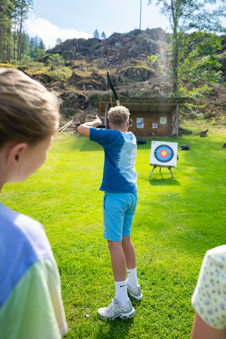 Junge zielt mit Bogen auf Zielscheibe, zwei Kinder schauen zu | © TVB/Laura Passenbrunner