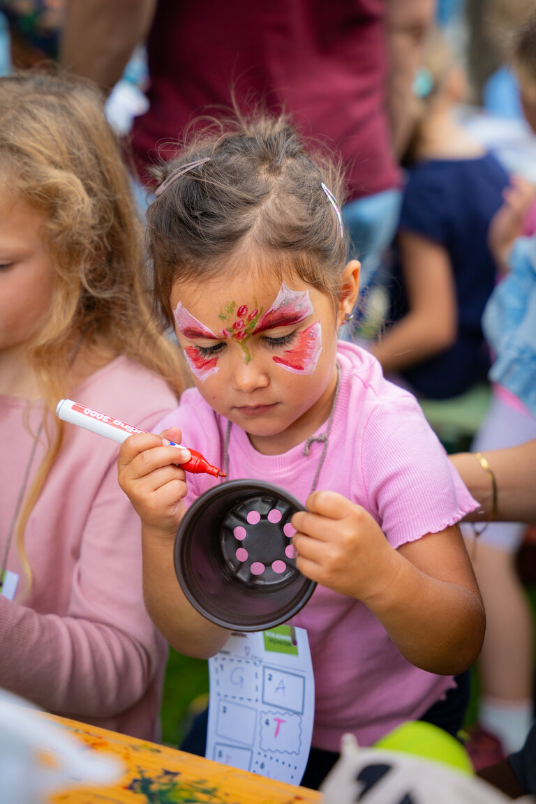 Kind mit Schmetterlingsschminke bemalt Blumentopf beim Kinderbastelprogramm. | © TVB/Laura Passenbrunner