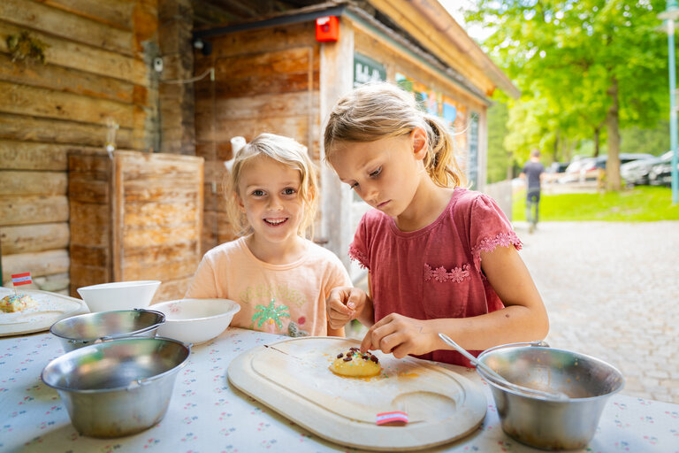 Zwei Mädchen verzieren Gebäck am Tisch vor der Waldhäuslalm. | © TVB/Laura Passenbrunner