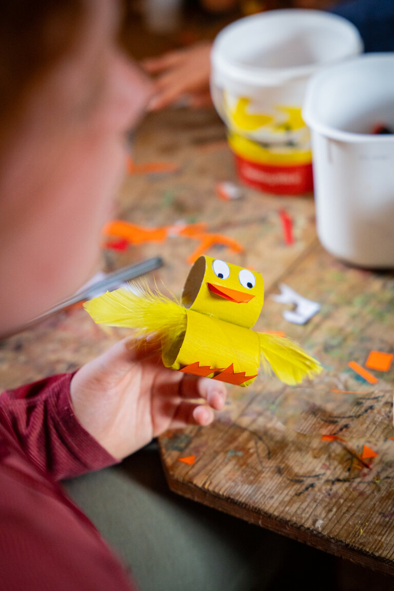 Kind zeigt selbstgebasteltes gelbes Küken aus Papprollen mit Federn und Wackelaugen. | © TVB/Laura Passenbrunner