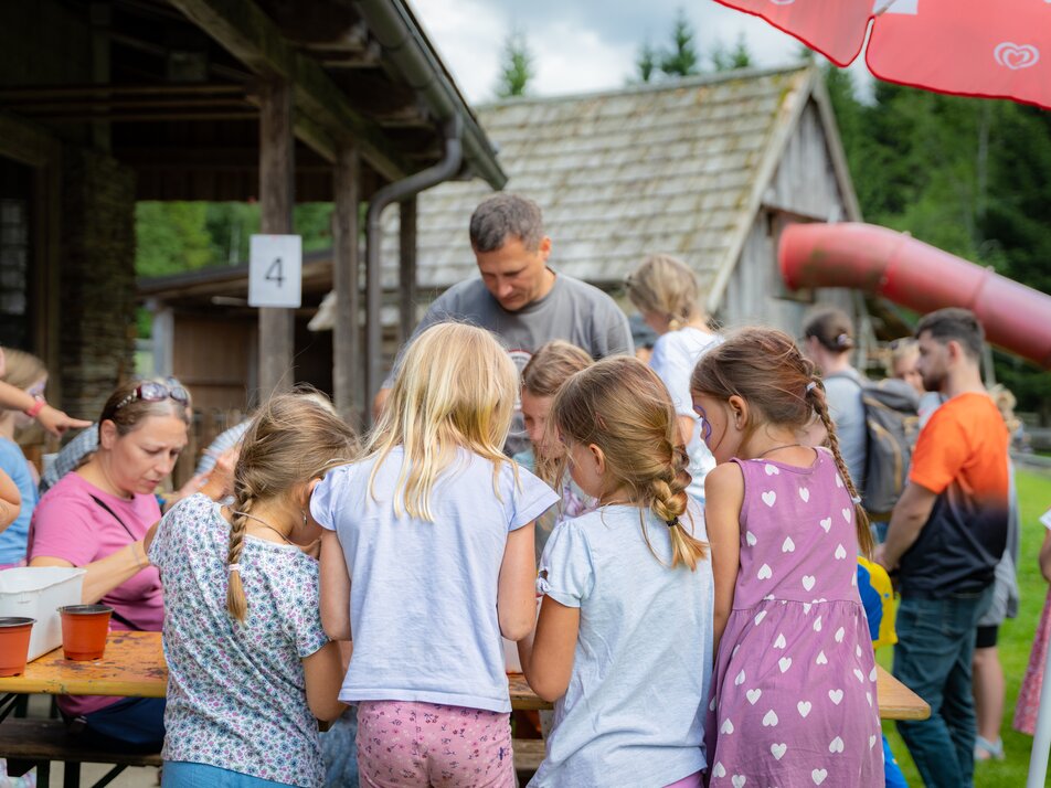 Kinder basteln gemeinsam an einem Tisch im Freien vor einer Almhütte beim Kinderprogramm. | © TVB/Laura Passenbrunner