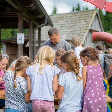Kinder basteln gemeinsam an einem Tisch im Freien vor einer Almhütte beim Kinderprogramm. | © TVB/Laura Passenbrunner