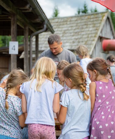 Kinder basteln gemeinsam an einem Tisch im Freien vor einer Almhütte beim Kinderprogramm. | © TVB/Laura Passenbrunner