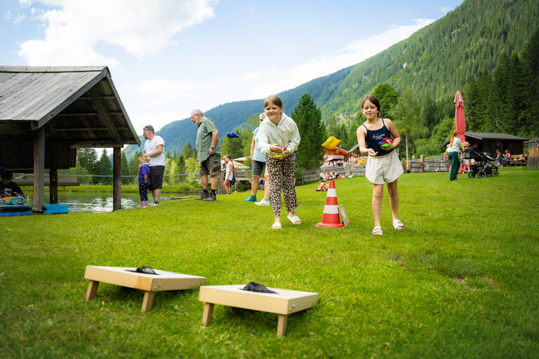 Zwei Mädchen werfen Säckchen bei einem Wurfspiel auf Wiese mit Bergkulisse. | © TVB/Laura Passenbrunner