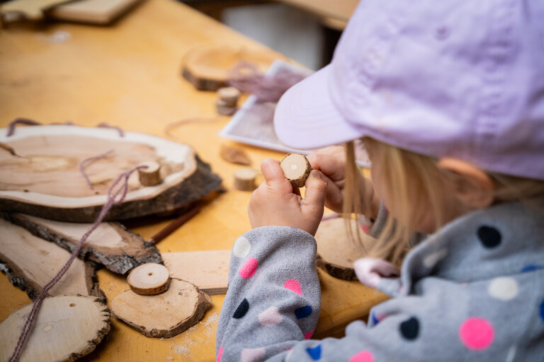 Kind bastelt mit Holzscheiben und Kordel bei der Kindertischlerei. | © TVB/Laura Passenbrunner