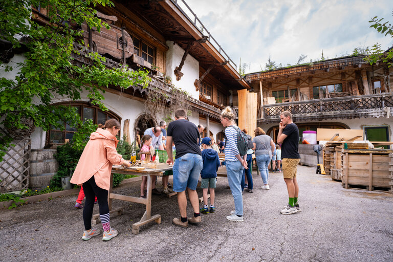 Kinder und Erwachsene werkeln gemeinsam im Hof einer Tischlerei an Holzprojekten. | © TVB/Laura Passenbrunner