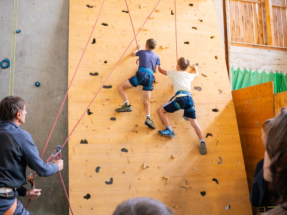 Zwei Kinder klettern gesichert an einer Indoor-Kletterwand, Erwachsene sichern und schauen zu. | © TVB/Laura Passenbrunner