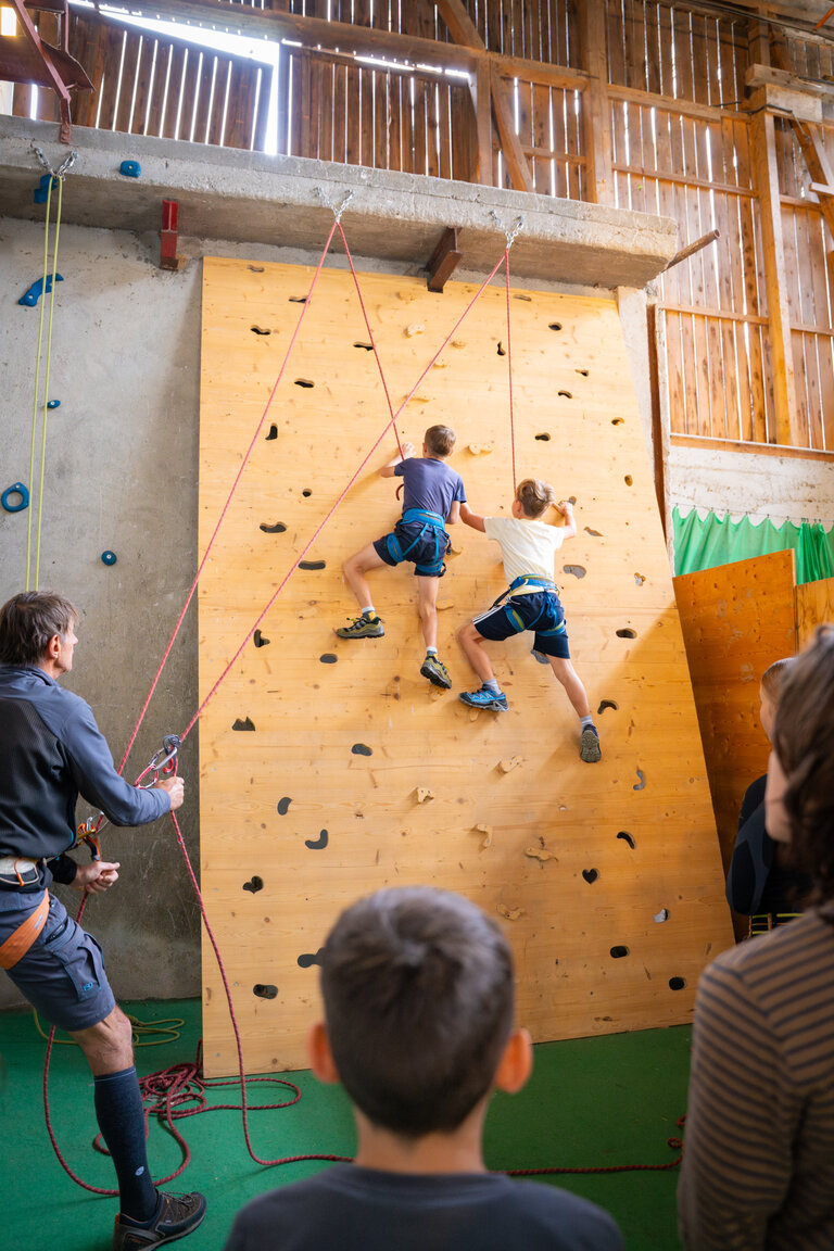Zwei Kinder klettern gesichert an einer Indoor-Kletterwand, Erwachsene sichern und schauen zu. | © TVB/Laura Passenbrunner