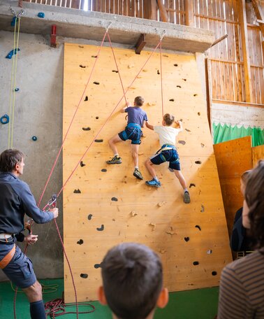 Zwei Kinder klettern gesichert an einer Indoor-Kletterwand, Erwachsene sichern und schauen zu. | © TVB/Laura Passenbrunner