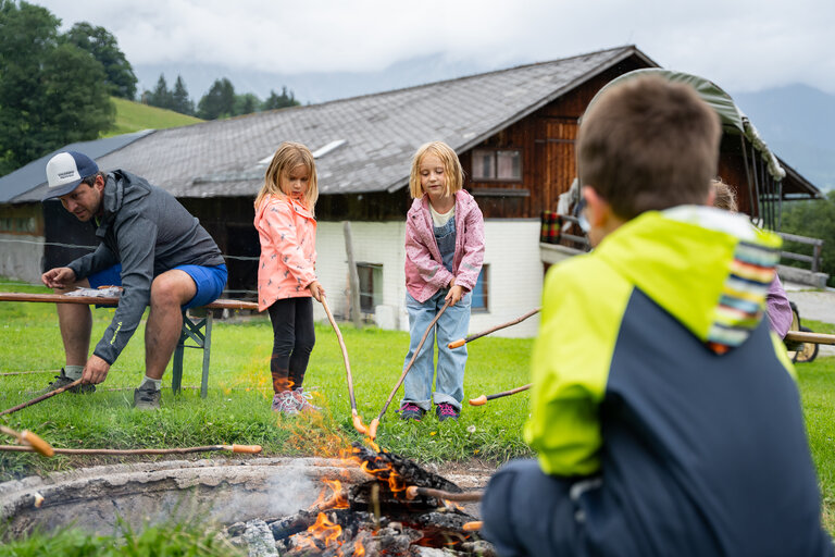 Kinder rösten Würstel über einem Lagerfeuer vor einem Bauernhaus. | © TVB/Laura Passenbrunner