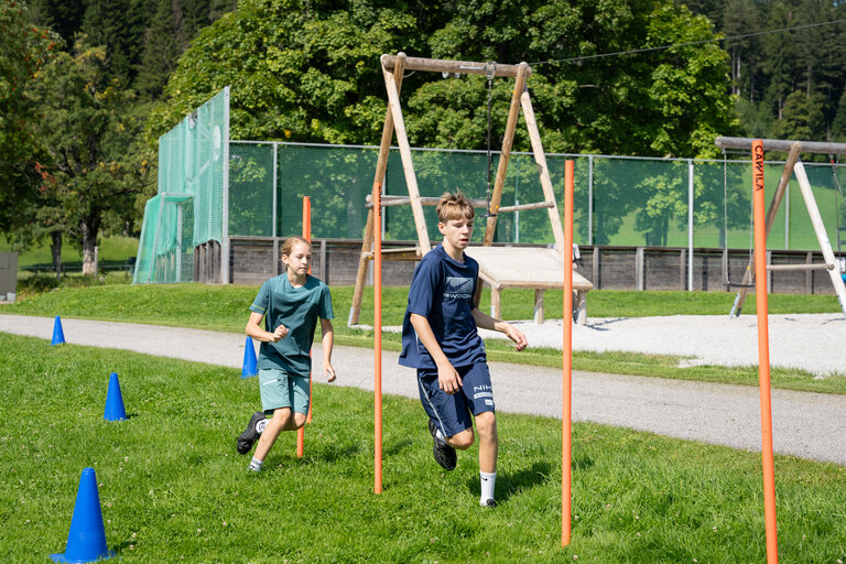 „Zwei Kinder laufen während eines Laserbiathlon-Parcours über eine grüne Wiese in Ramsau am Dachstein.“ | © TVB/Laura Passenbrunner