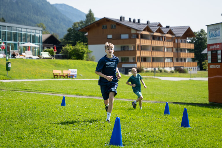 Zwei Kinder laufen im Rahmen des Kinderprogramms einen Biathlon-Parcours auf einer Wiese mit markierten Hütchen ab. | © TVB/Laura Passenbrunner