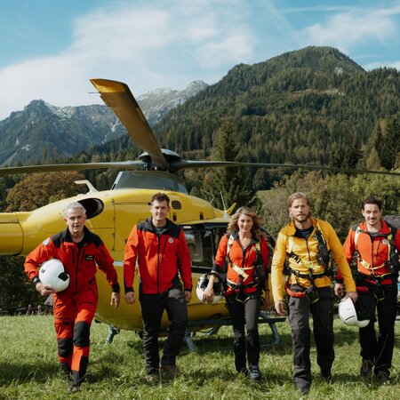 Fünf Personen in Bergrettungsoutfit marschieren auf einer Wiese. Im Hintergrund steht ein Helikopter.  | © ZDF_2024_17. Staffel