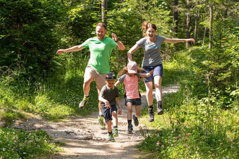 Eine Familie springt glücklich in die Luft auf einem Wanderweg  | © Lorenz Maser 