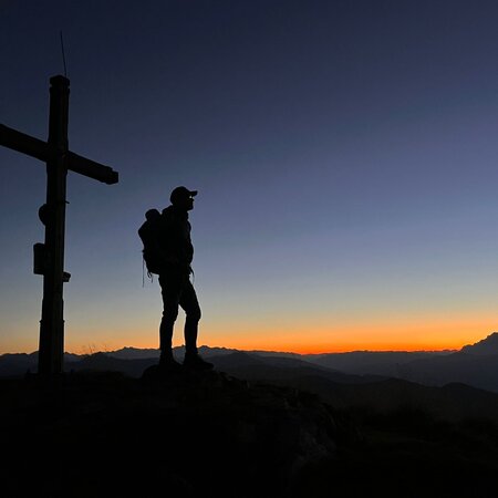 Ein Wanderer der bei Abenddämmerung am Gipfelkreuz steht | © Herbert Raffalt 