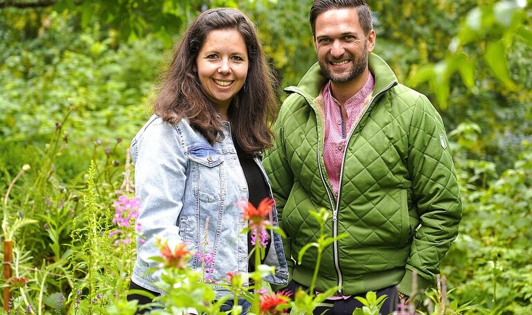 Kräuterexpertin Andrea Percht und Moderator Richard Deutinger posieren für ein Foto im Kräutergarten, aufgenommen | © ServusTV / Brigitte Erhart / Degn Film