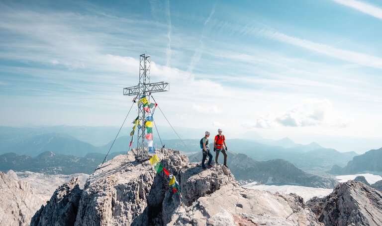 Eine Frau und ein Mann stehen in Kletterausrüstung am Gipfel und genießen die Aussicht. | © Mathäus Gartner