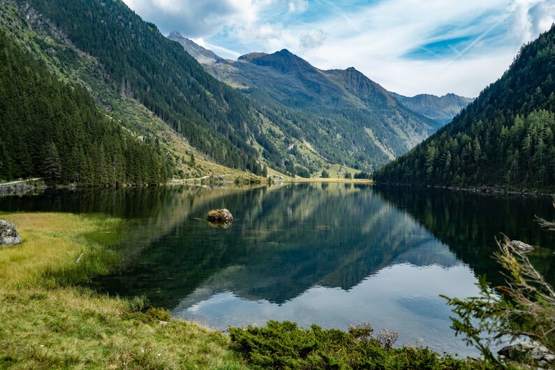 Blick auf den ruhigen Riesachsee inmitten eines grünen Hochtals, umgeben von bewaldeten Berghängen und einem dramatischen Gebirgsmassiv im Hintergrund. | © Christine Höflehner